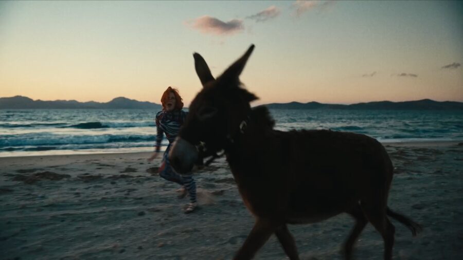 A donkey walking a beach at dusk, a figure following behind