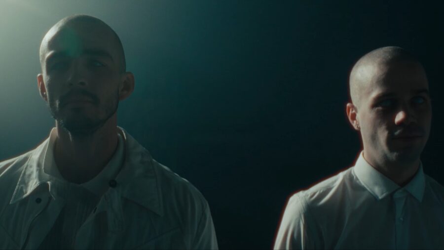 Two men standing apart in a dark room, each half-lit
