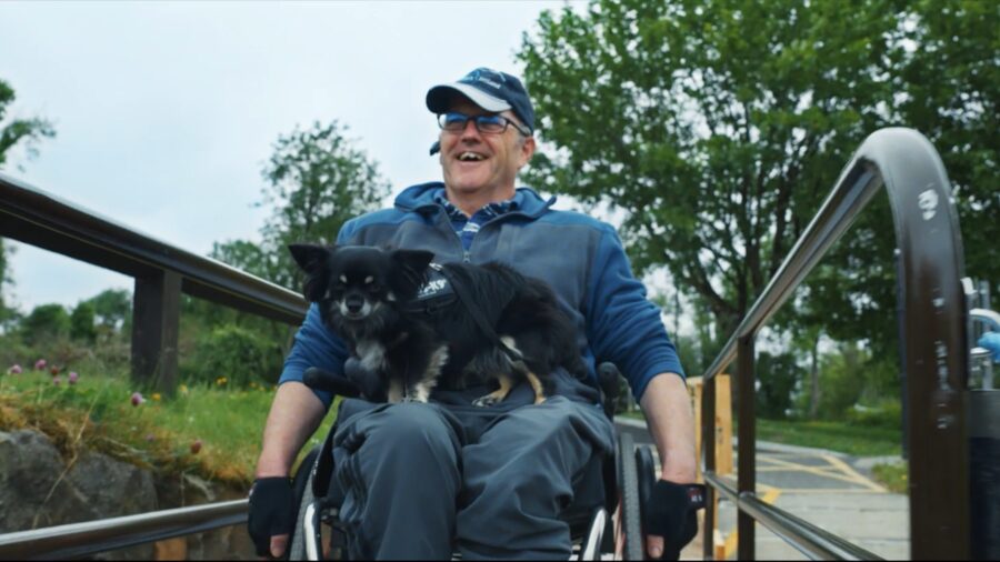 A man in a wheelchair with his dog at the top of a riverside ramp