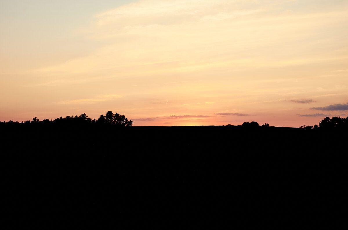 Sun setting over a dark tree line
