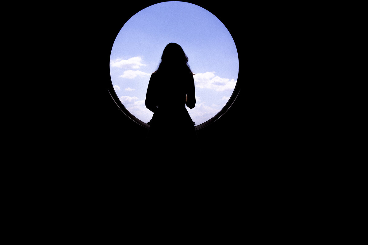 Silhouette of a figure seen through a round window against open sky
