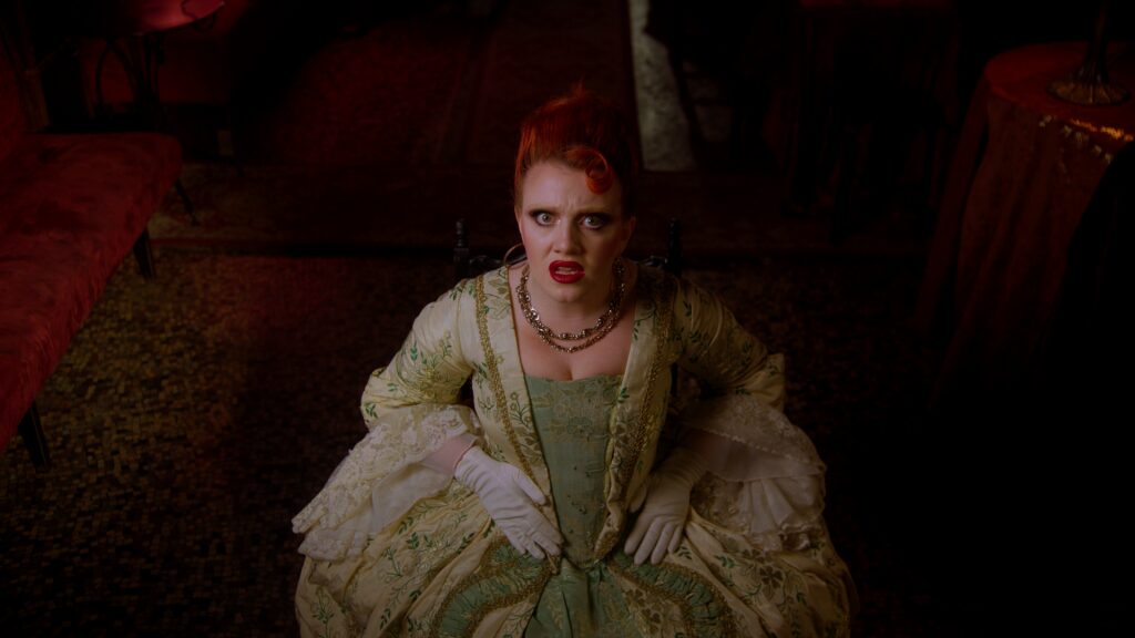 CMAT in period costume, red hair piled high, lit by candlelight in a dark room