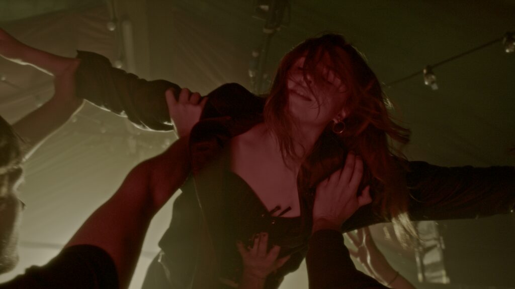 A woman crowd surfing at a gig, hair lit red by stage lighting