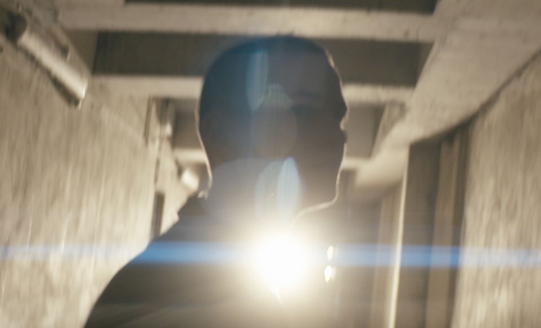 A silhouetted figure backlit by a bright light in a concrete corridor