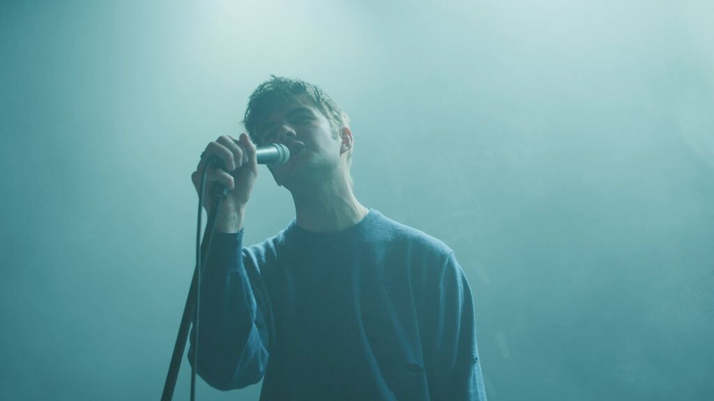 A singer at the microphone in teal stage light, shot close from the side