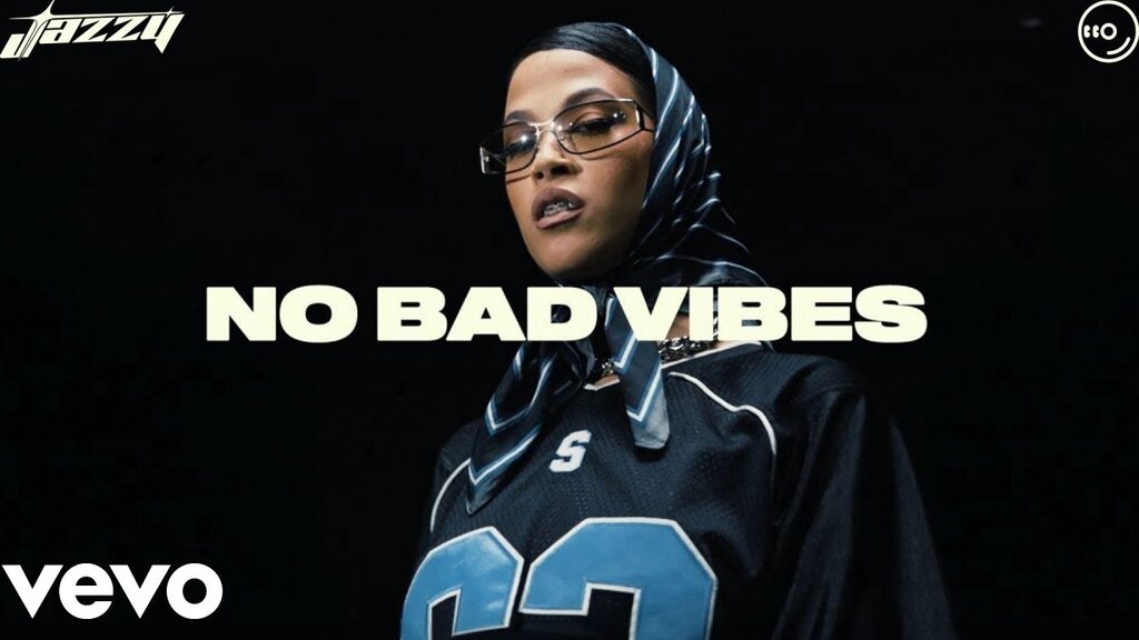 Jazzy in a printed headscarf and a navy jersey against black, the words No Bad Vibes across the frame