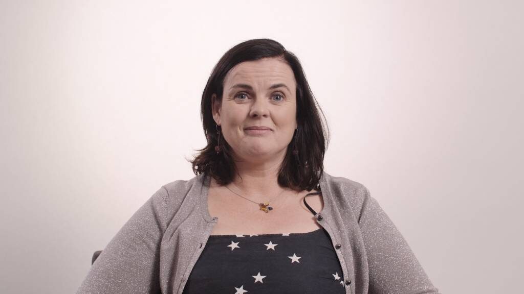 A woman speaking to camera against a plain light backdrop